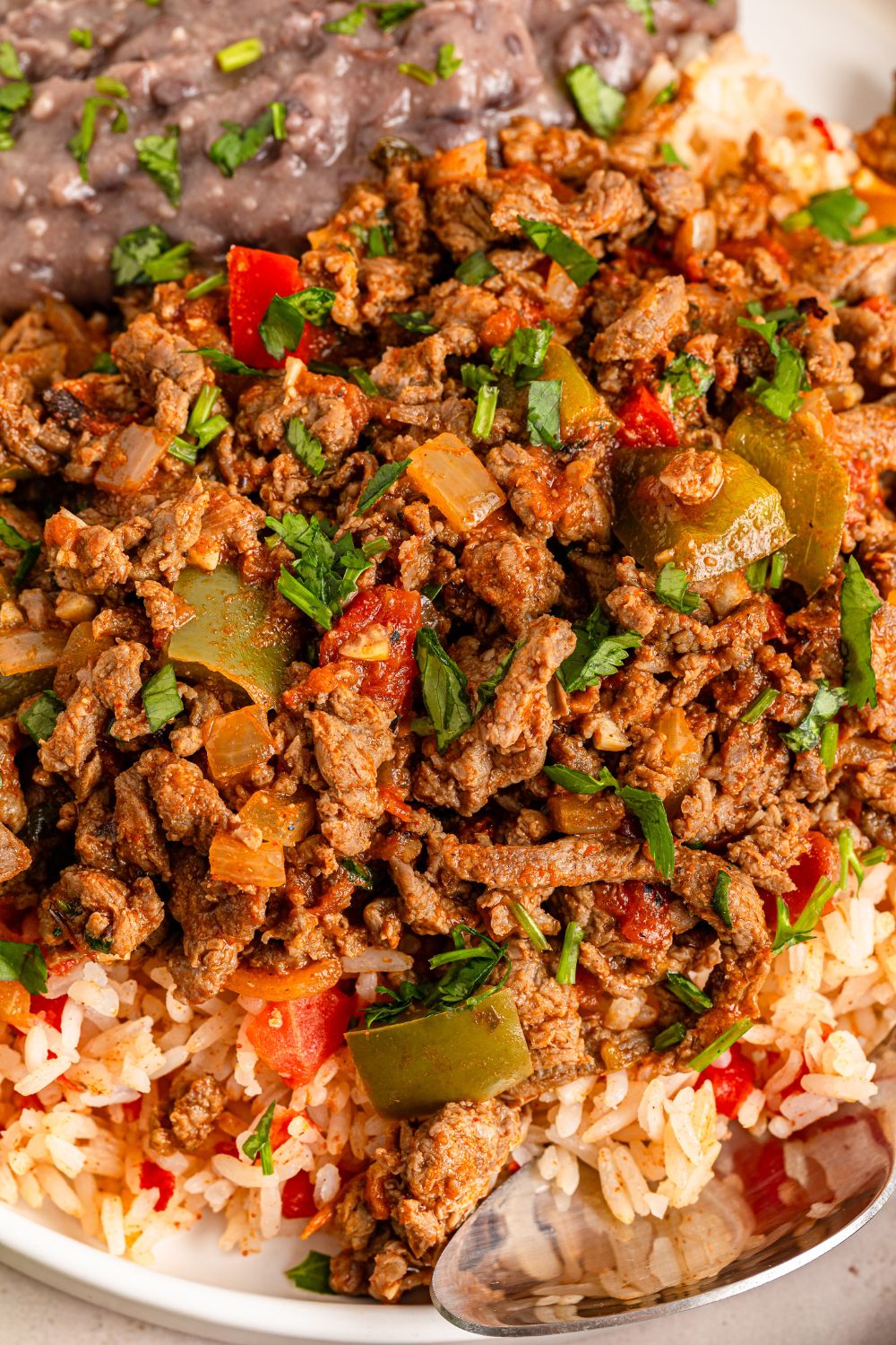 Carne Picada in a bowl with rice and mashed beans with a spoon around the bowl