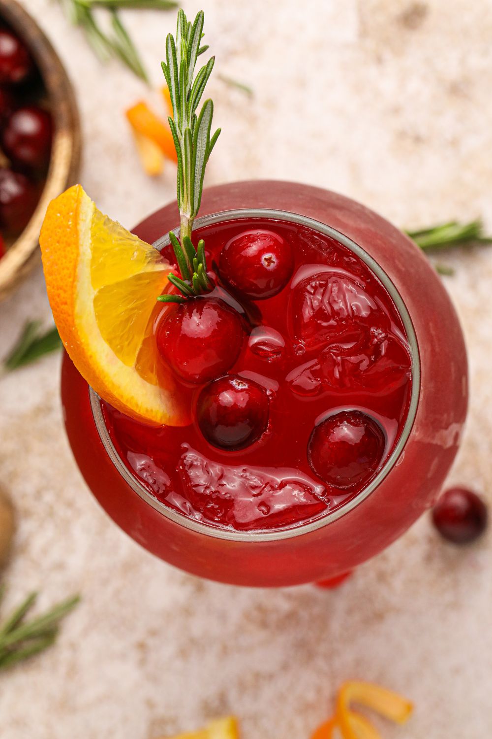 Cranberry Whiskey Sour on table with an overhead look into the glass with an orange slice and cranberries in the glass with ice 