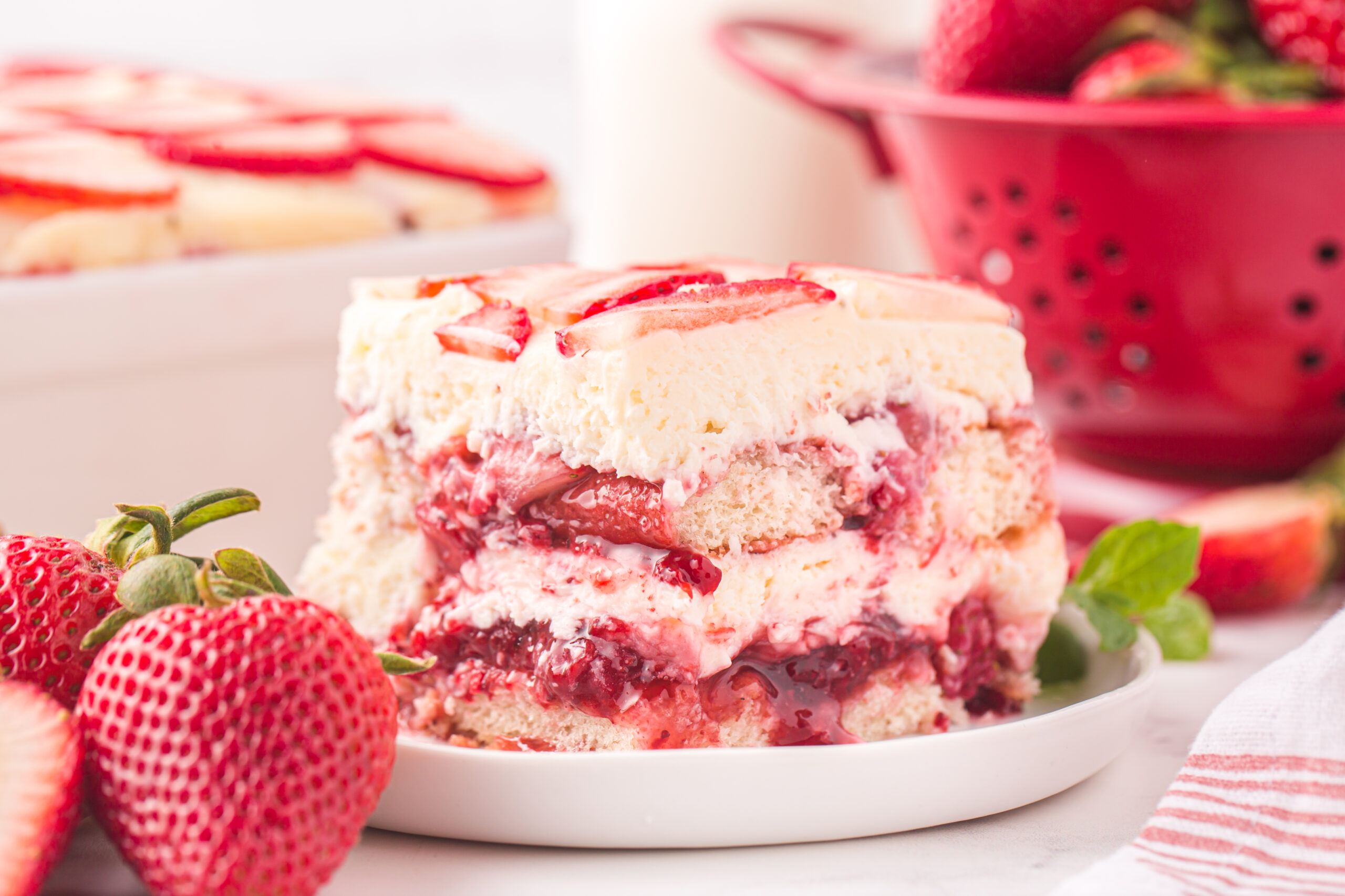 side view of Strawberry Tiramisu on a white plate surrounded by fresh strawberries