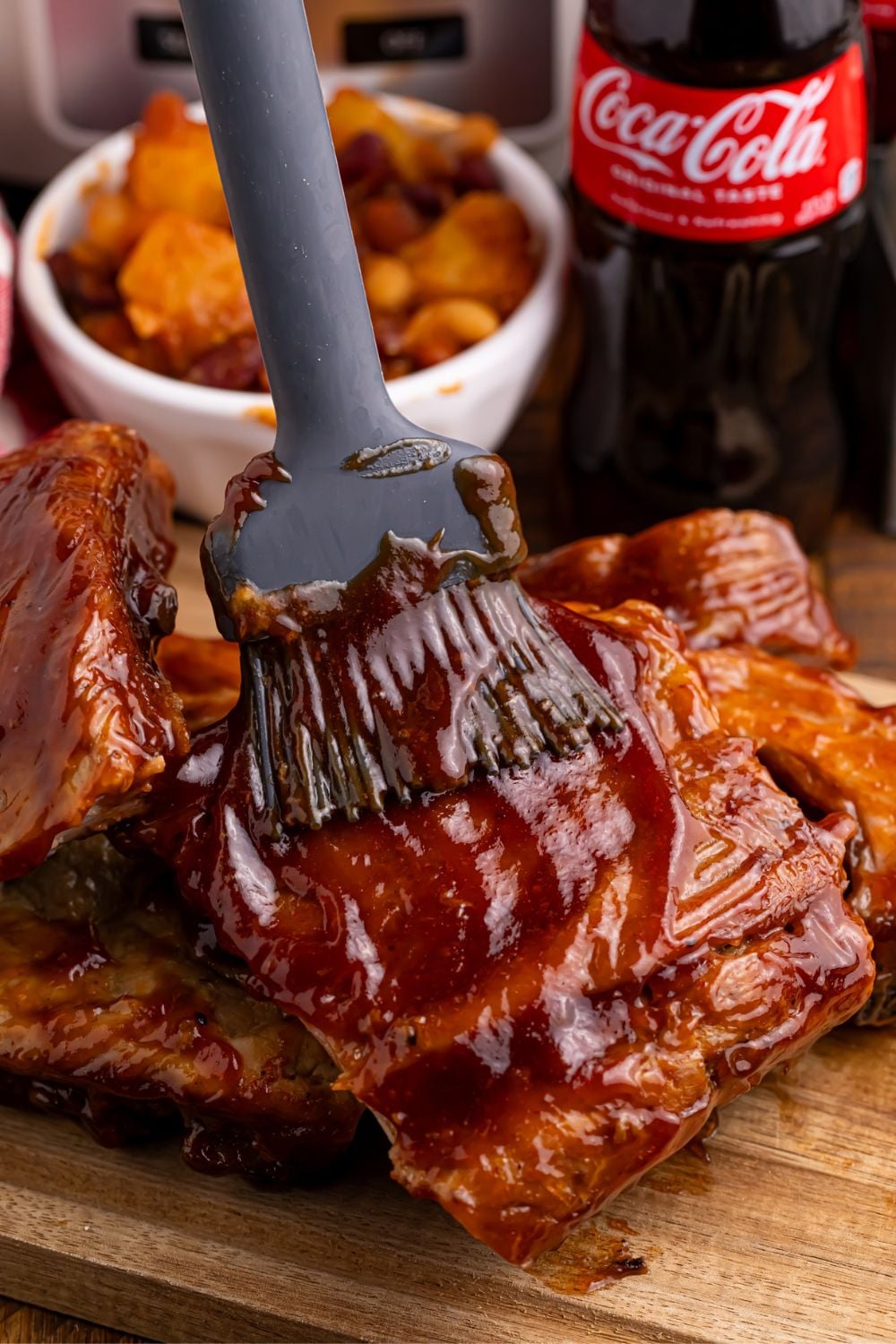 basting Slow Cooker Coca Cola Ribs on a wooden cutting board on table 