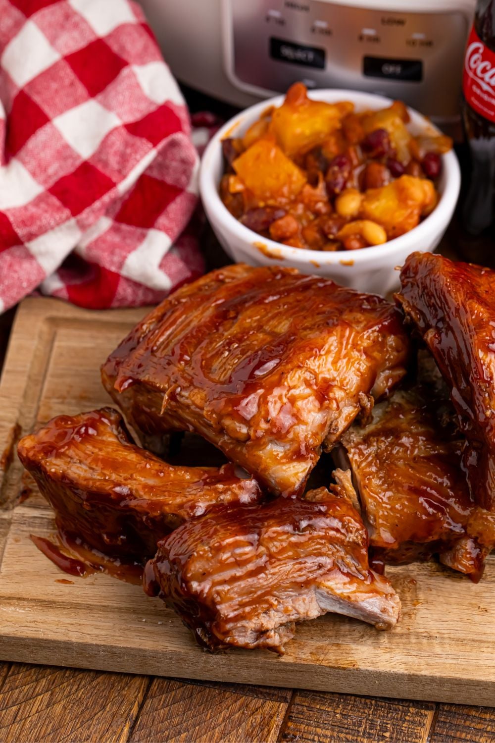 Slow Cooker Coca Cola Ribs on a wooden cutting table with a bowl of bbq beans 