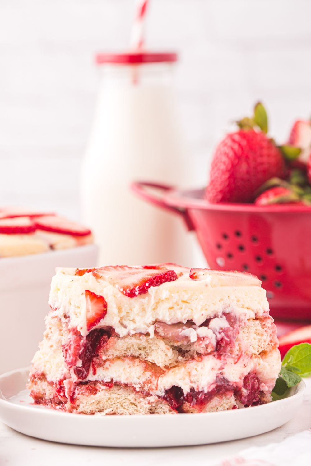 strainer of strawberries, glass of milk, and plate with tiramisu