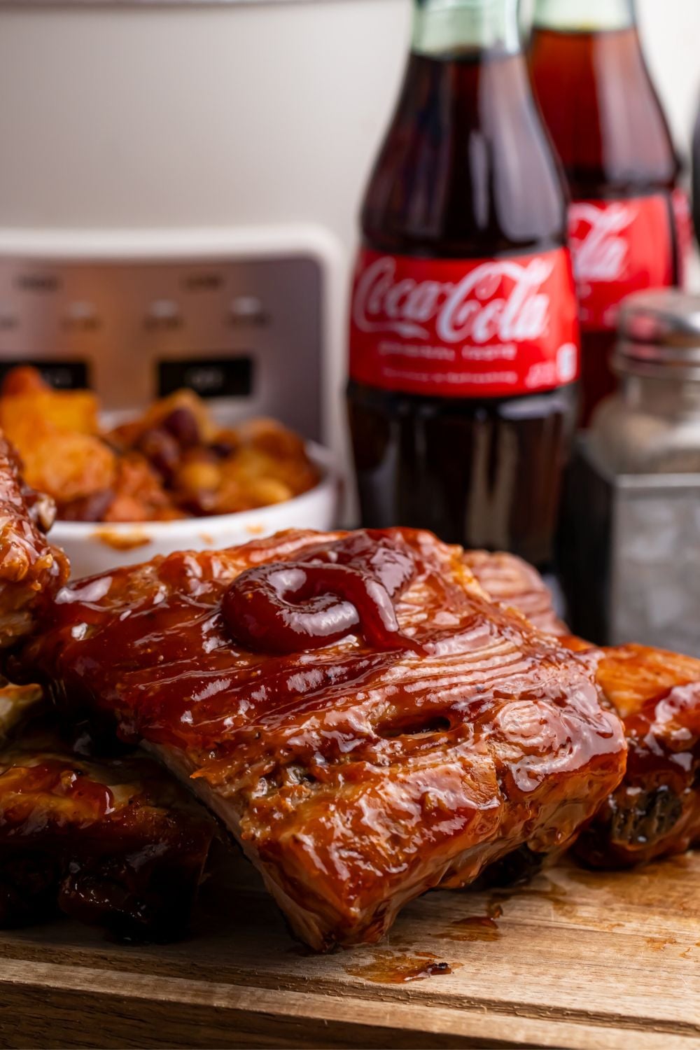Slow Cooker Coca Cola Ribs stacked on platter, with bottles of coke in the background 