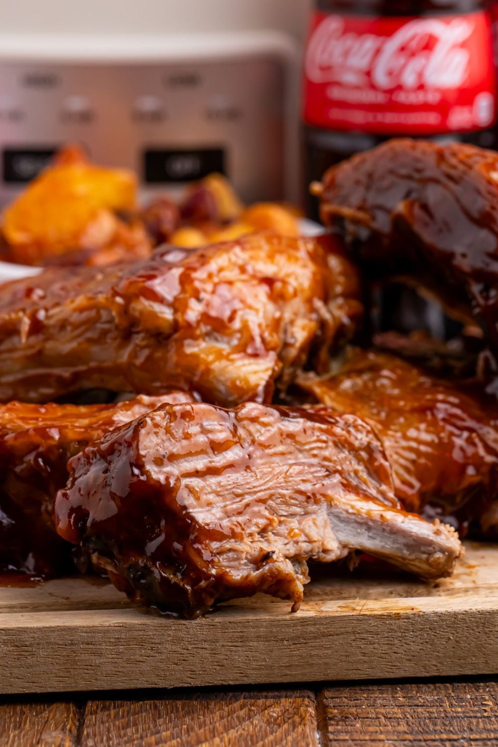 Slow Cooker Coca Cola Ribs stacked on top of each other on cutting board with slow cooker in the background 