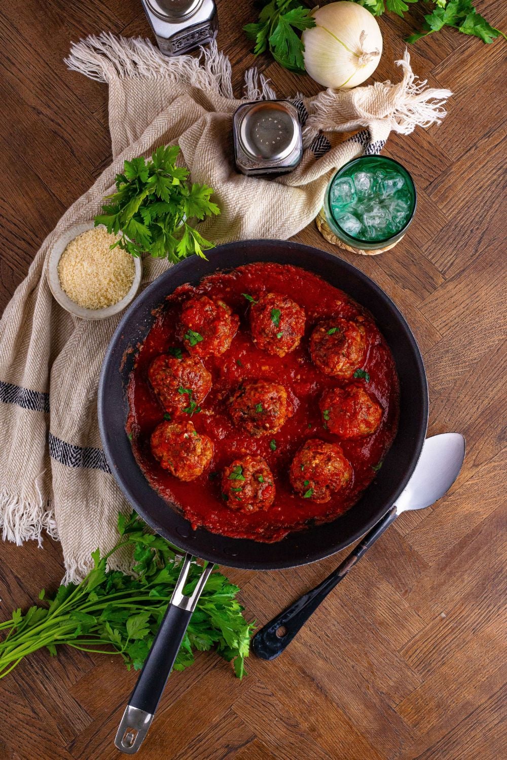 Classic Italian Meatballs in a skillet with garnishes around the pan 
