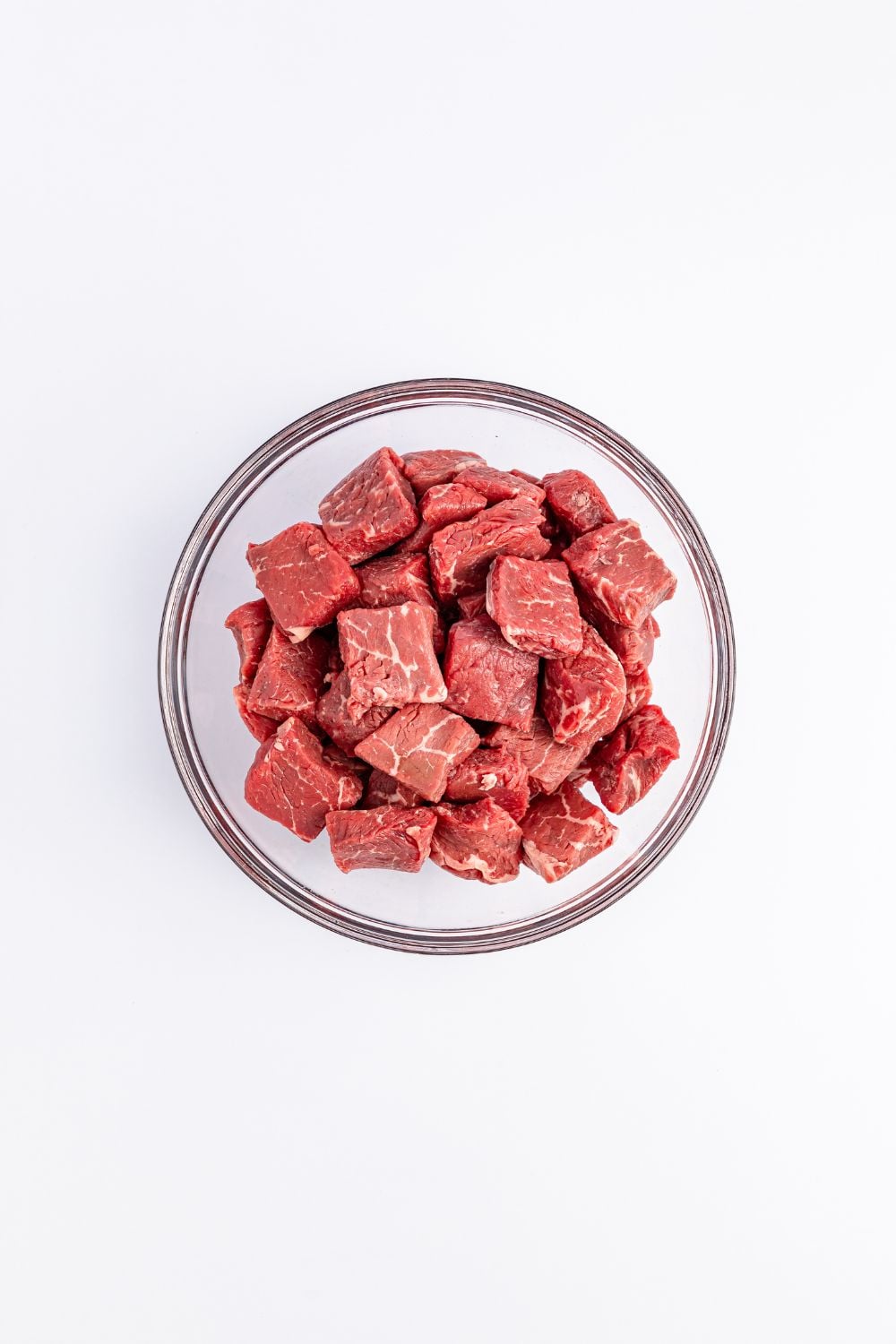 raw cubed steak in a glass bowl on white counter