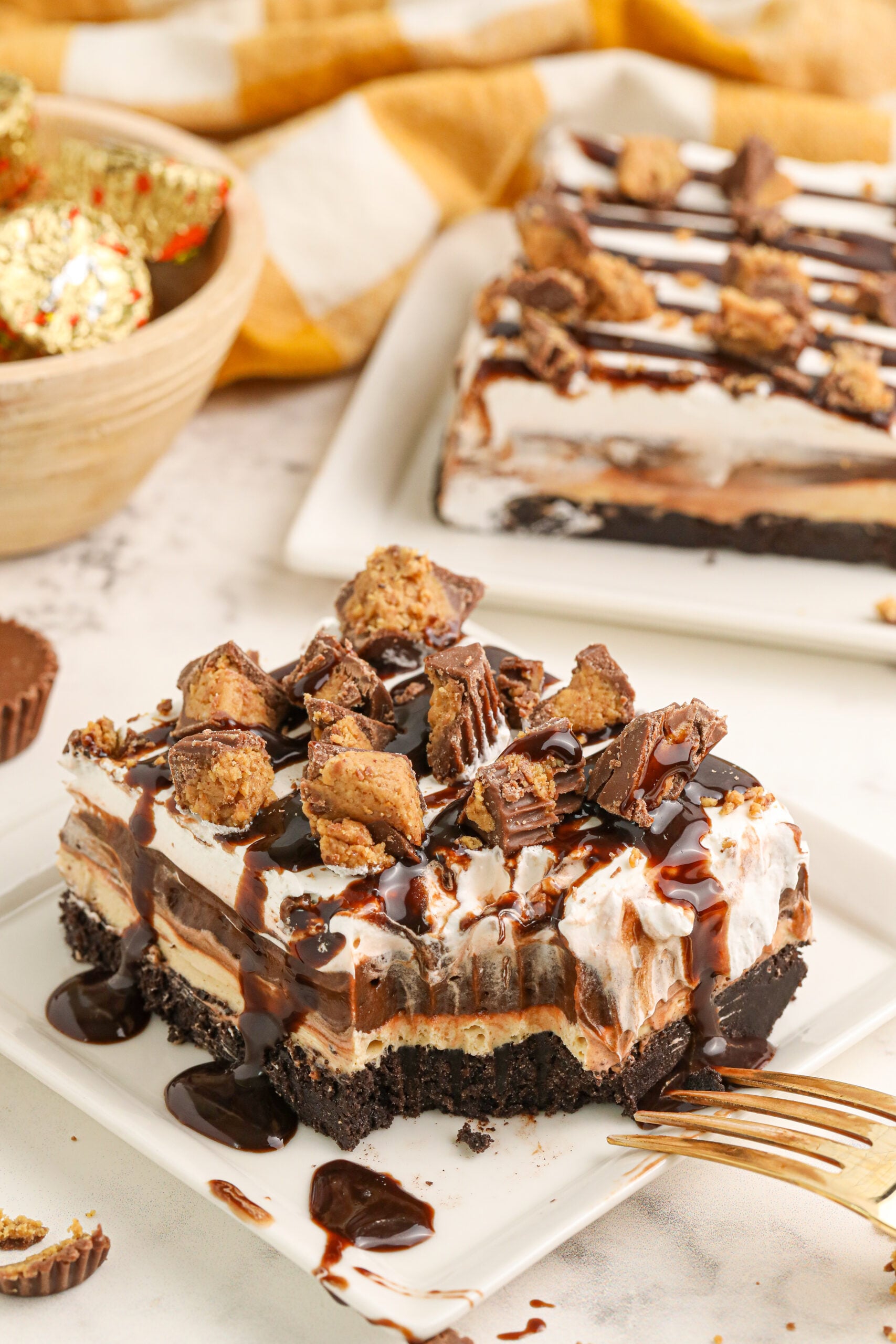 Reeses Lasagna on a white plate with one bite taken out of it topped with crumbled reeses cups
