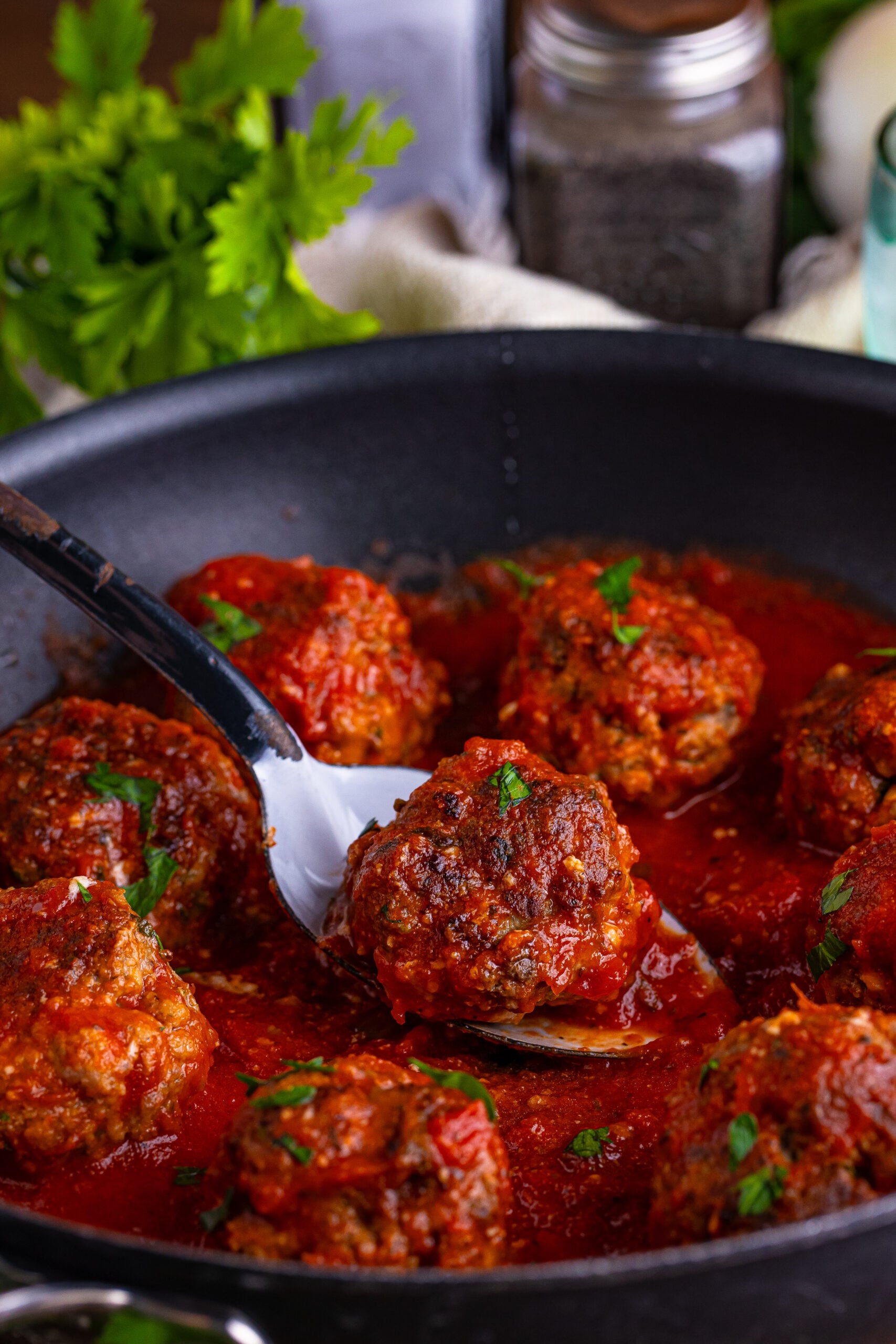 italian meatballs in a skillet with a spoon lifting one up 