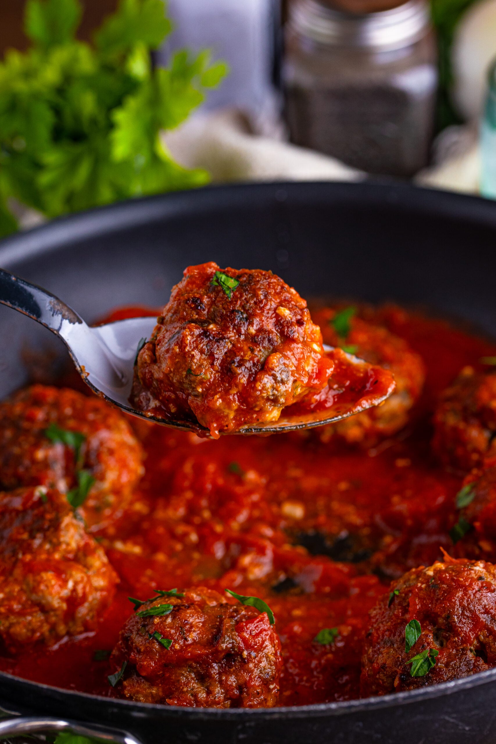 Classic Italian Meatballs in a pan with salt and pepper to the side, parsley, and other ingredients 