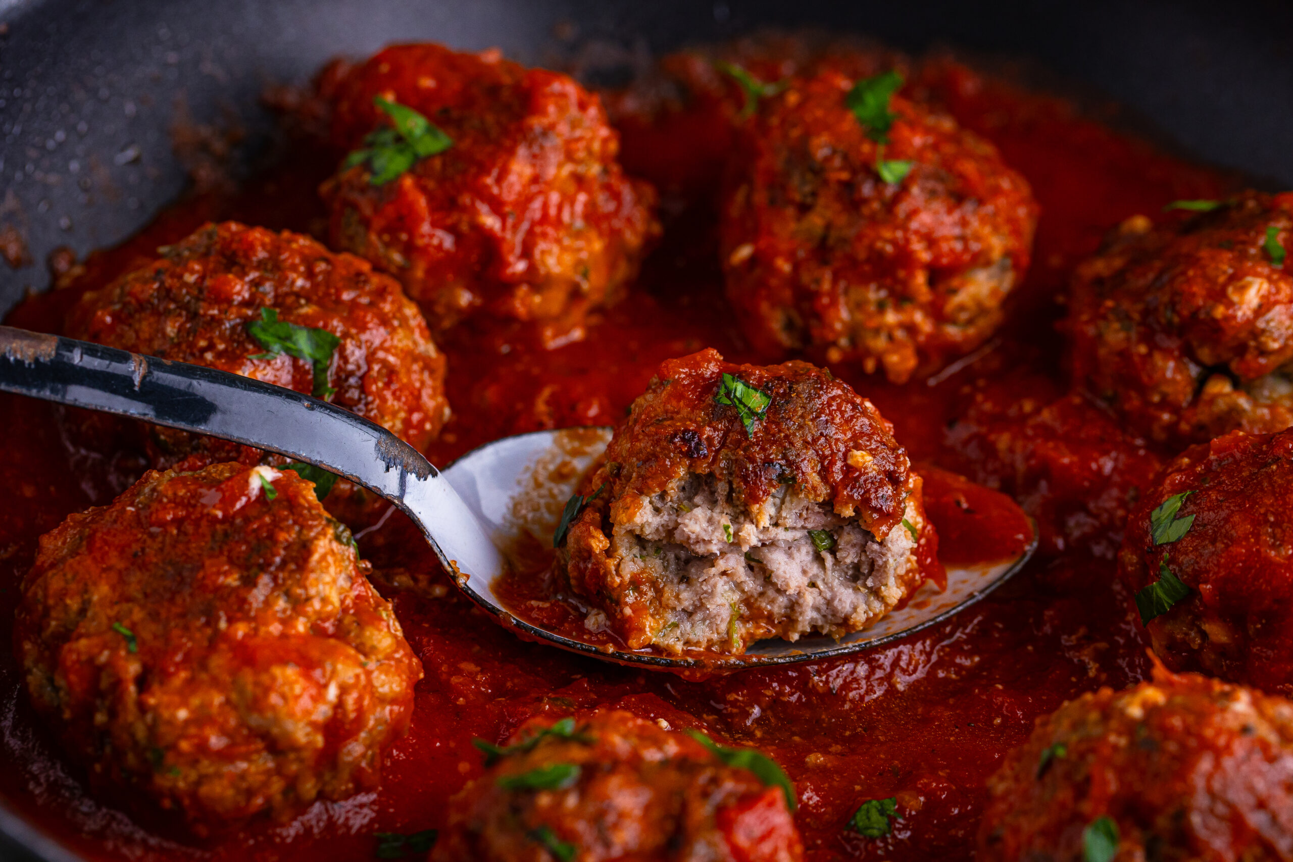 Classic Italian Meatball with a bite taken out of it close up in a pan with a marinara sauce drizzled on top 