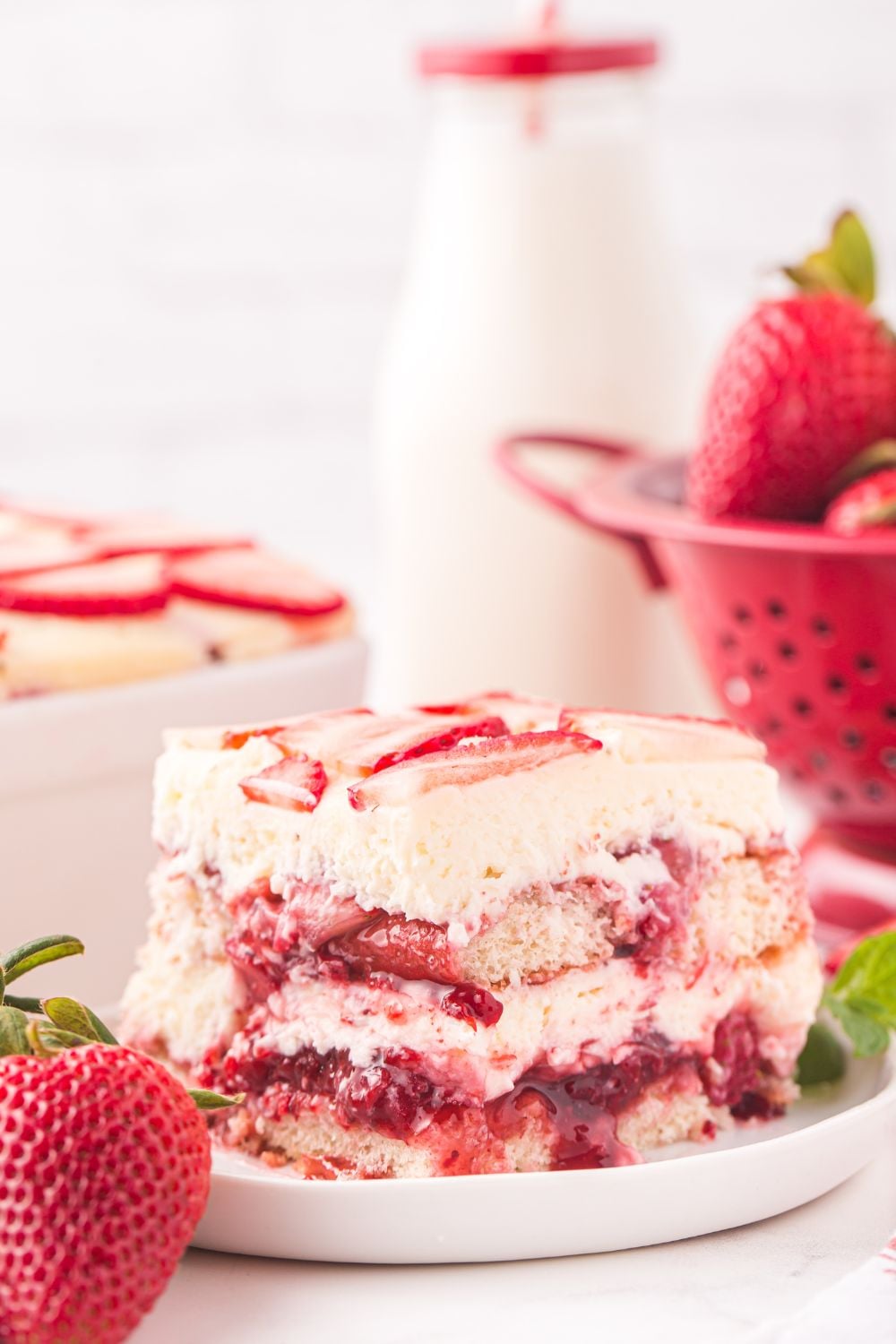 Strawberry Tiramisu sliced and placed on a plate with berries, and a glass of milk behind the plate