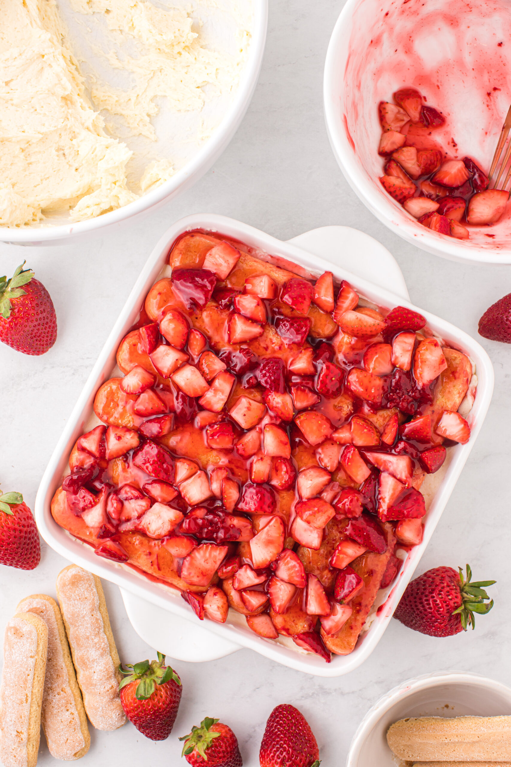 Strawberry Tiramisu on table with a bowl of mascarpone filling and a bowl of strawberries