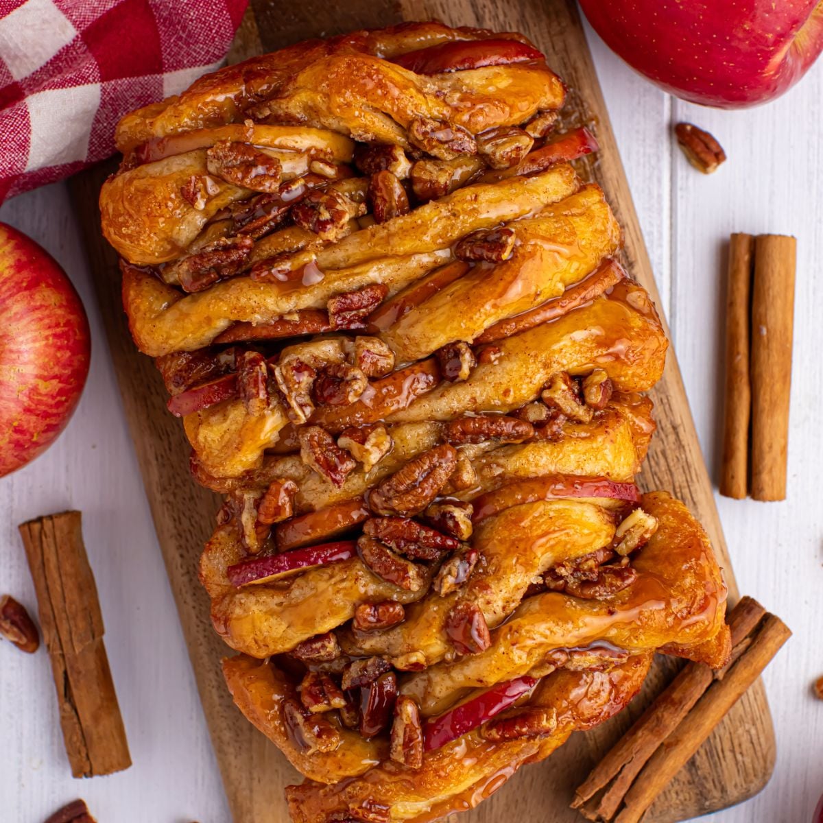 Apple Pie Pull Apart Bread on a cutting board on table with cinnamon sticks and apples around the serving tray