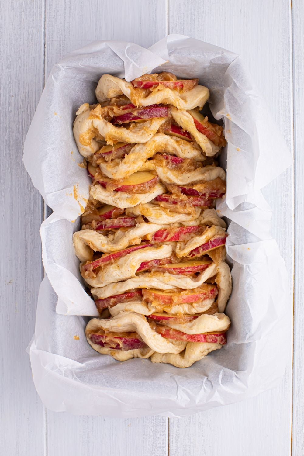 Apple Pie Pull Apart Bread in the loaf pan full of the cinnamon mixture and apples in between layers of dough