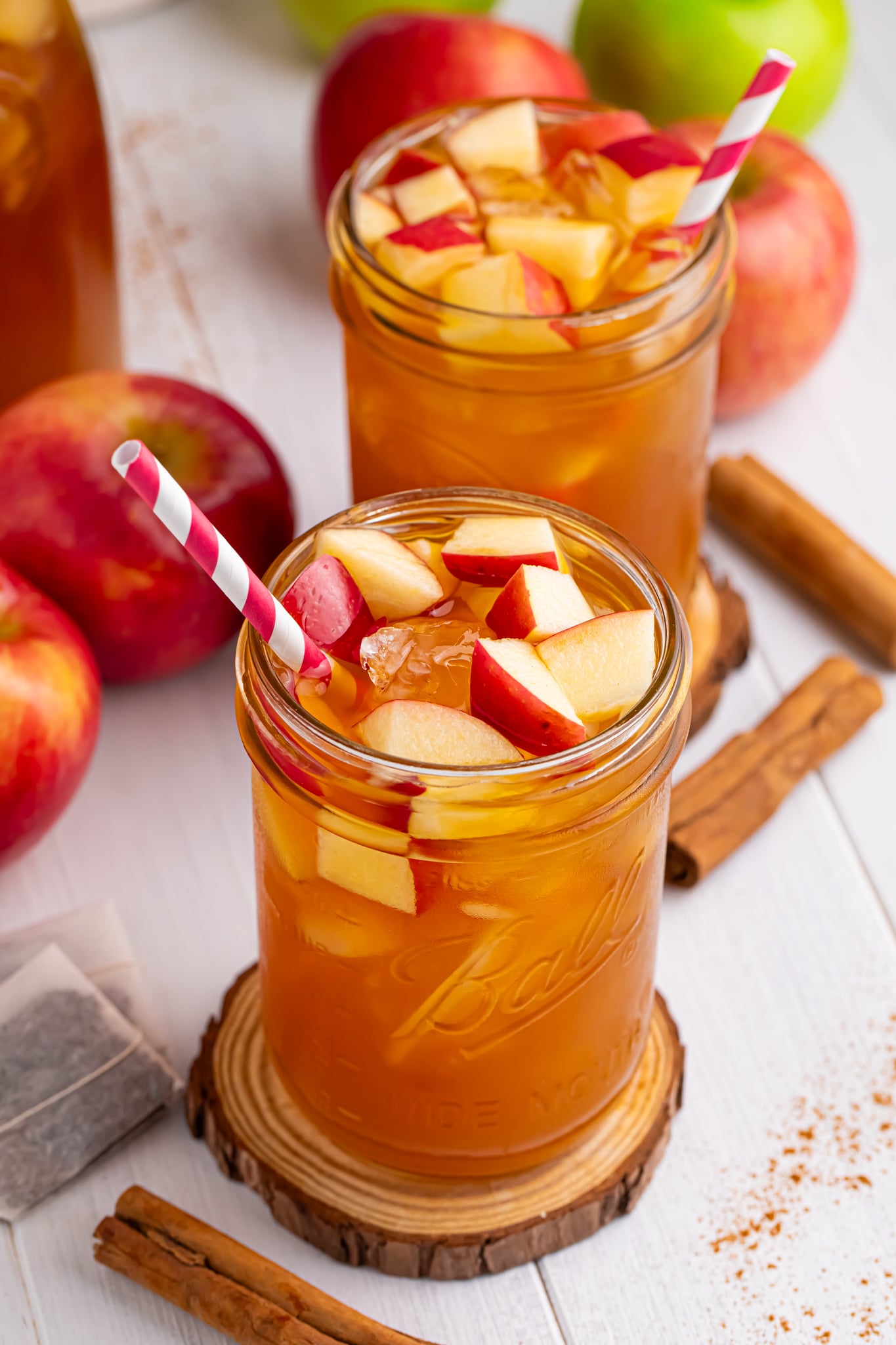 apple cider iced tea in a glass with a shot of the glass with a straw in it and diced fresh apples with ice cubes