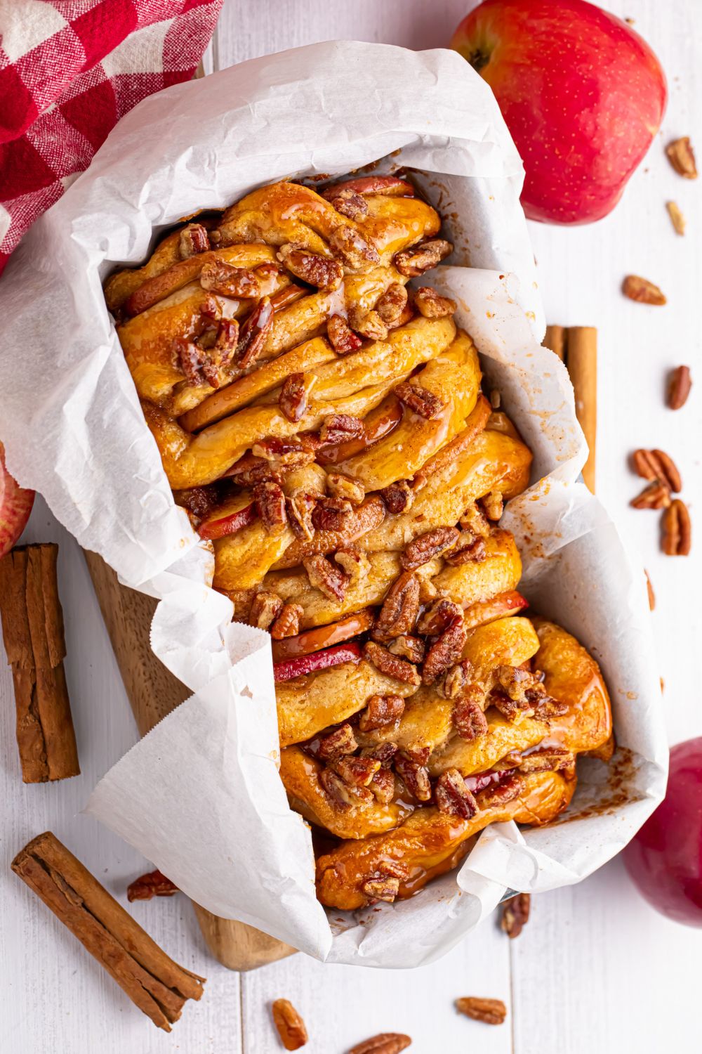 Apple Pie Pull Apart Bread in a pan sitting on the table with cinnamon sticks and cloves spread around on table with apples around it