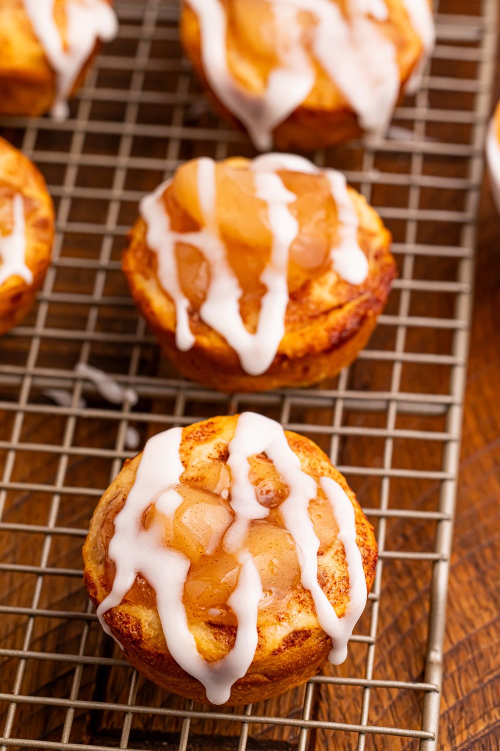 apple pie cups sitting on a wire cooling rack with the glaze drizzled on top