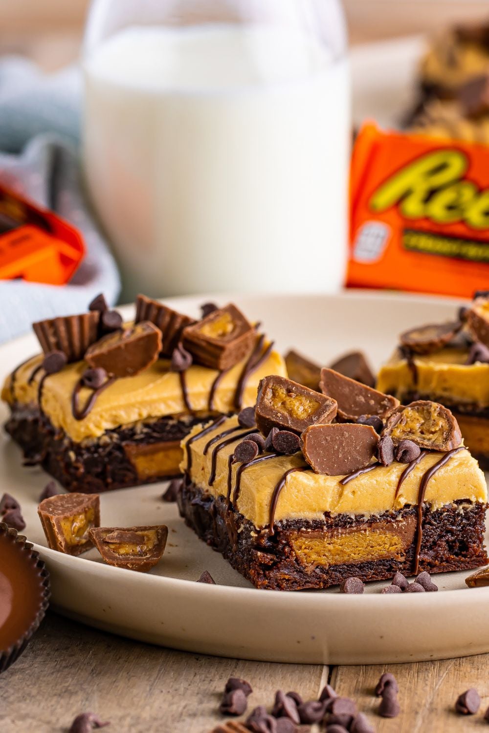 close up of brownies sliced into squares sitting on table with milk jug to side and Reeses scattered on plate