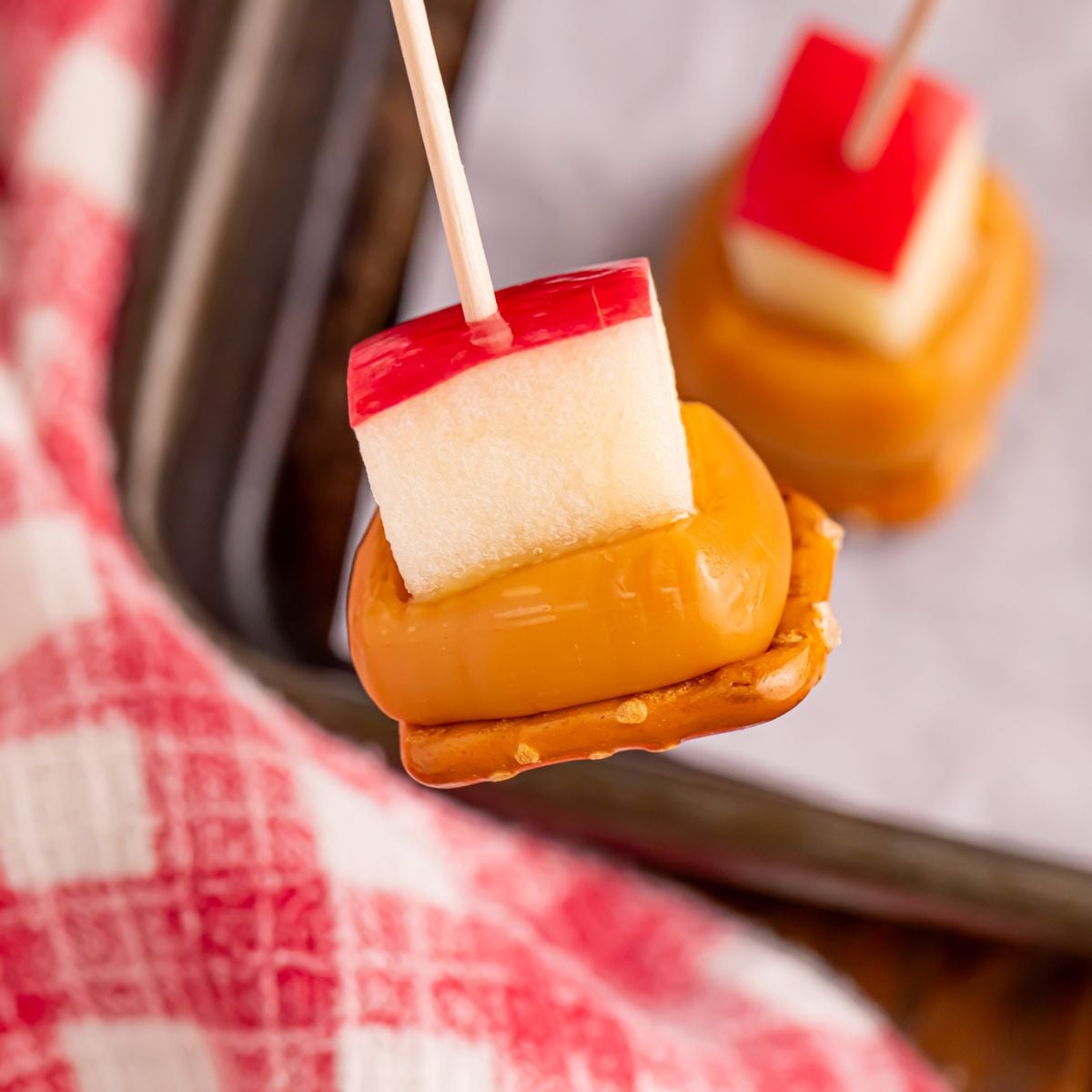 Caramel Apple Pretzel Bite on toothpick being held above pan on table