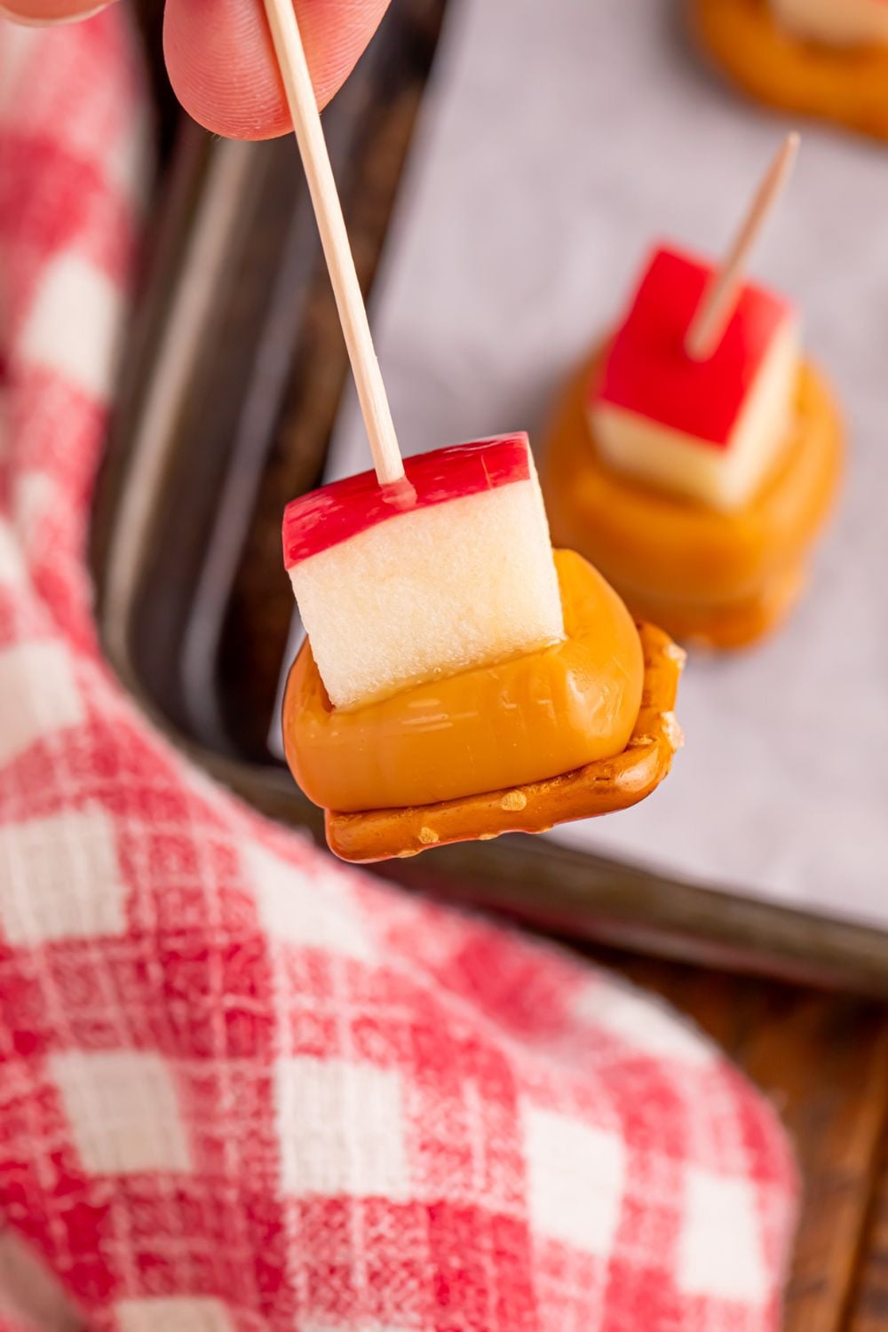 Caramel Apple Pretzel Bite being held by toothpick above tray with more