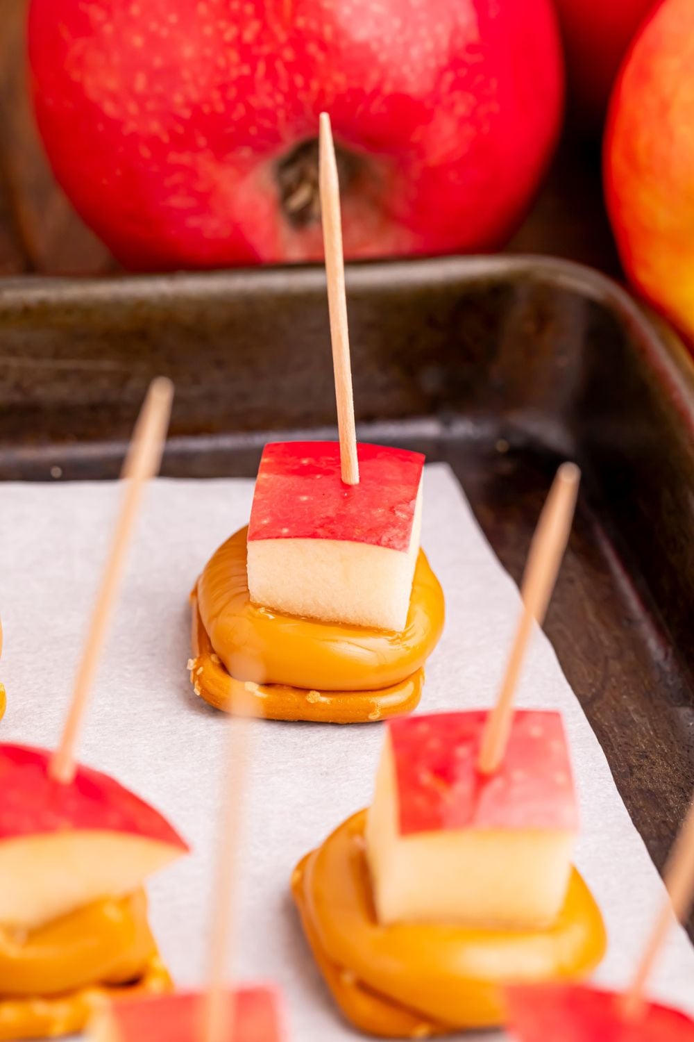 caramel apple treats with toothpicks poking in sitting on a baking tray on table