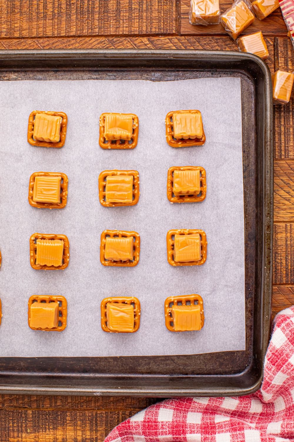 caramels sitting on top of pretzel squares on a baking tray