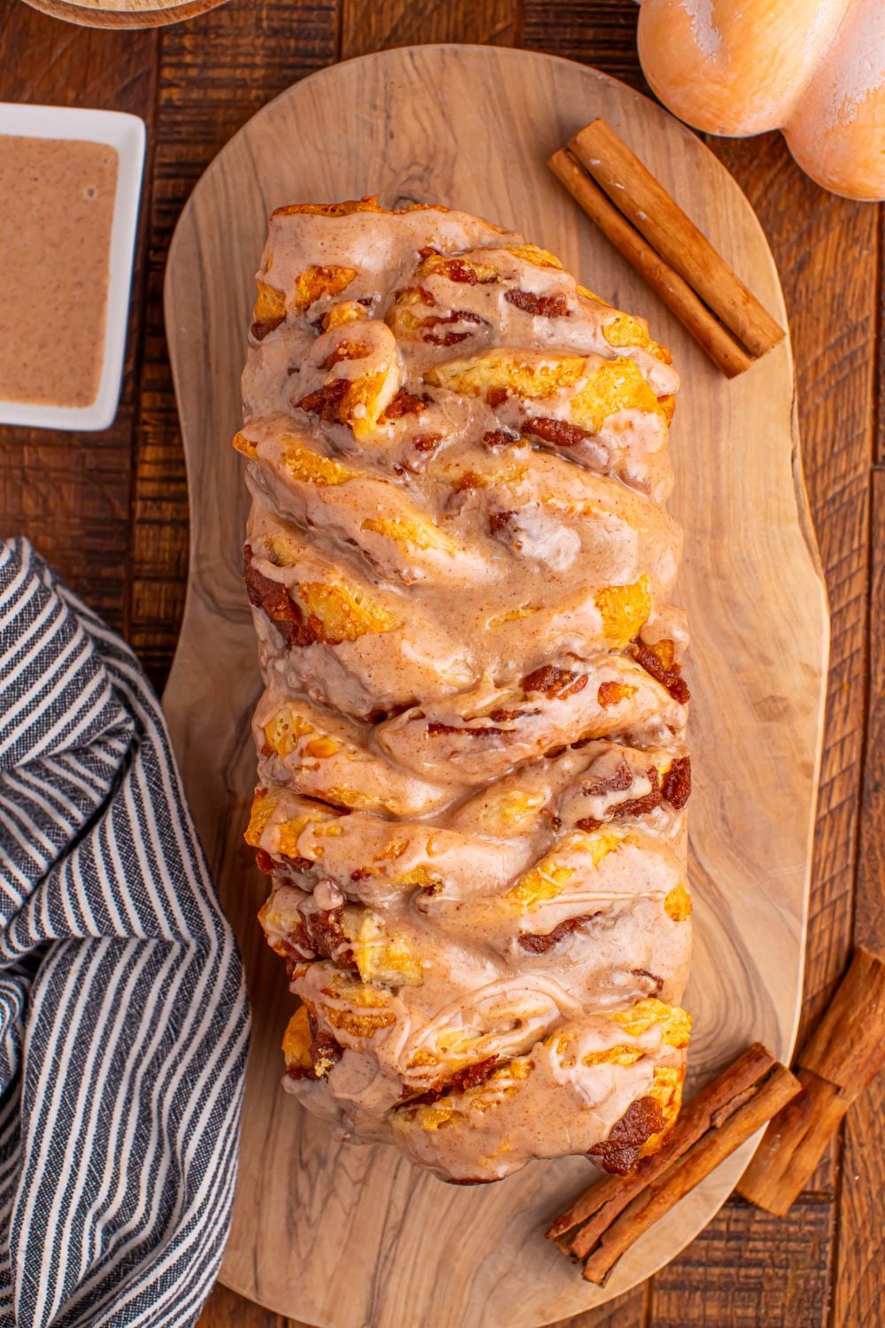 Pumpkin Pie Pull Apart Bread sitting on a table with a bowl of cinnamon sugar on side, and cinnamon sticks 