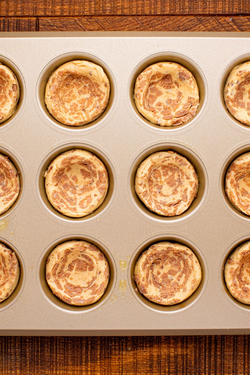 raw cinnamon rolls in a muffin tin with the centers pressed down for the apple pie cups