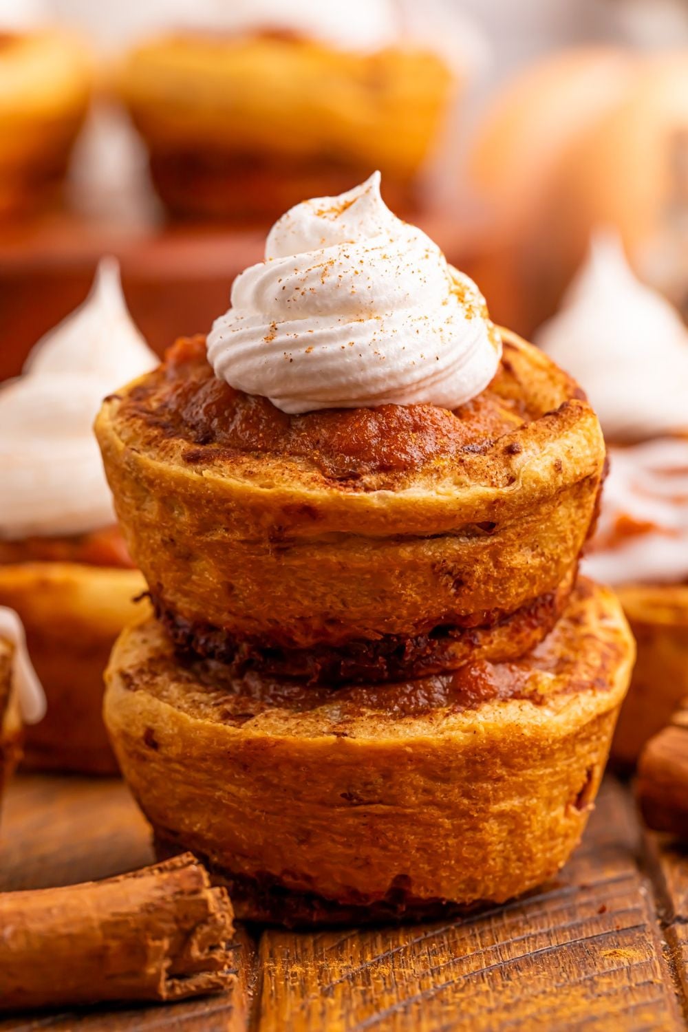 Pumpkin Pie Cinnamon Roll Cups on table with two stacked on top of each other and top one has a dollop of whipped cream on top