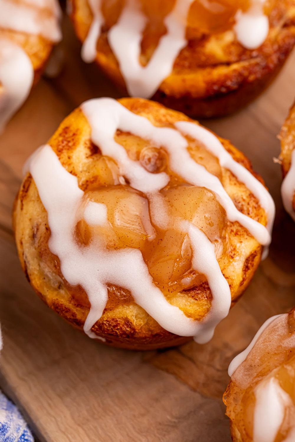 cinnamon rolls with apple pie filling in center and drizzled with icing, sitting on wooden cutting board on table