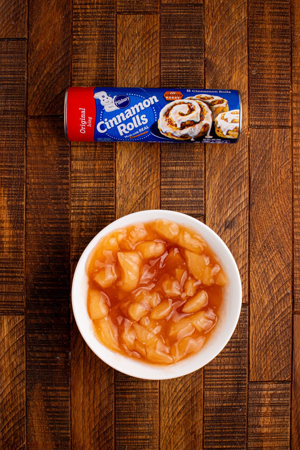 ingredients for apple pie cups on table. Bowl of apple pie filling and a roll of cinnamon rolls on table