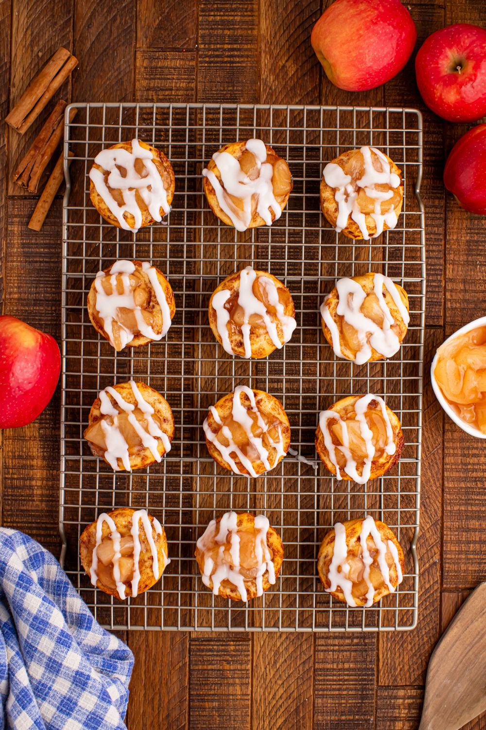 Easy Apple Pie Cups overhead look on table with a cooling rack with rows of apple pie cups on table with apples and cinnamon sticks around the rack