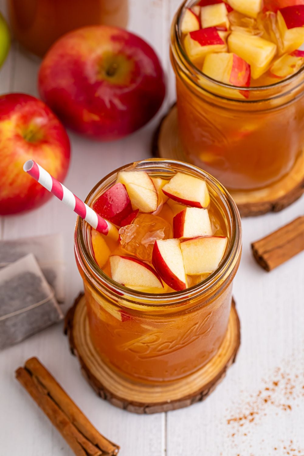 Apple Cider Iced Teas on table in mason jars with apples and cinnamon sticks spread over the table and fresh diced apples in the glasses