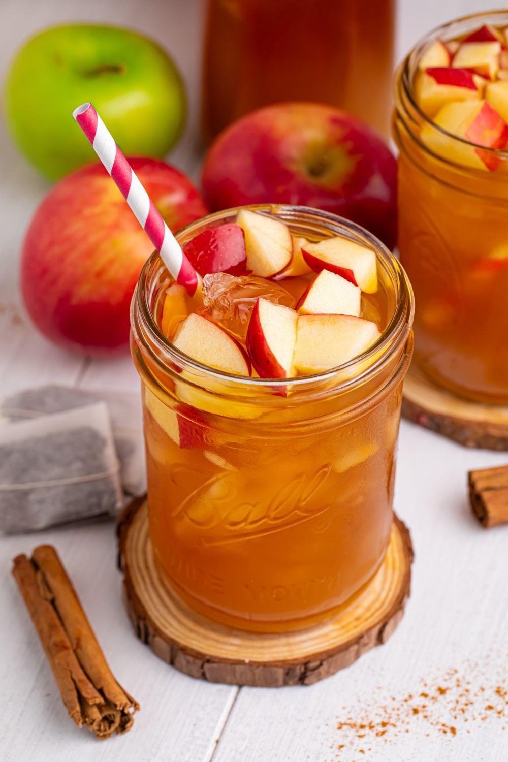 iced tea ciders in glasses with a cinnamon stick, tea bags, and apples on table around the glasses to show what flavors you will taste in the drink