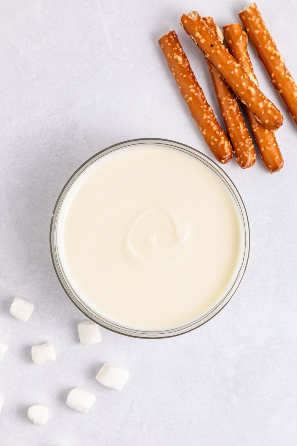 melted white chocolate in a bowl on table with broken pretzel rods on the side