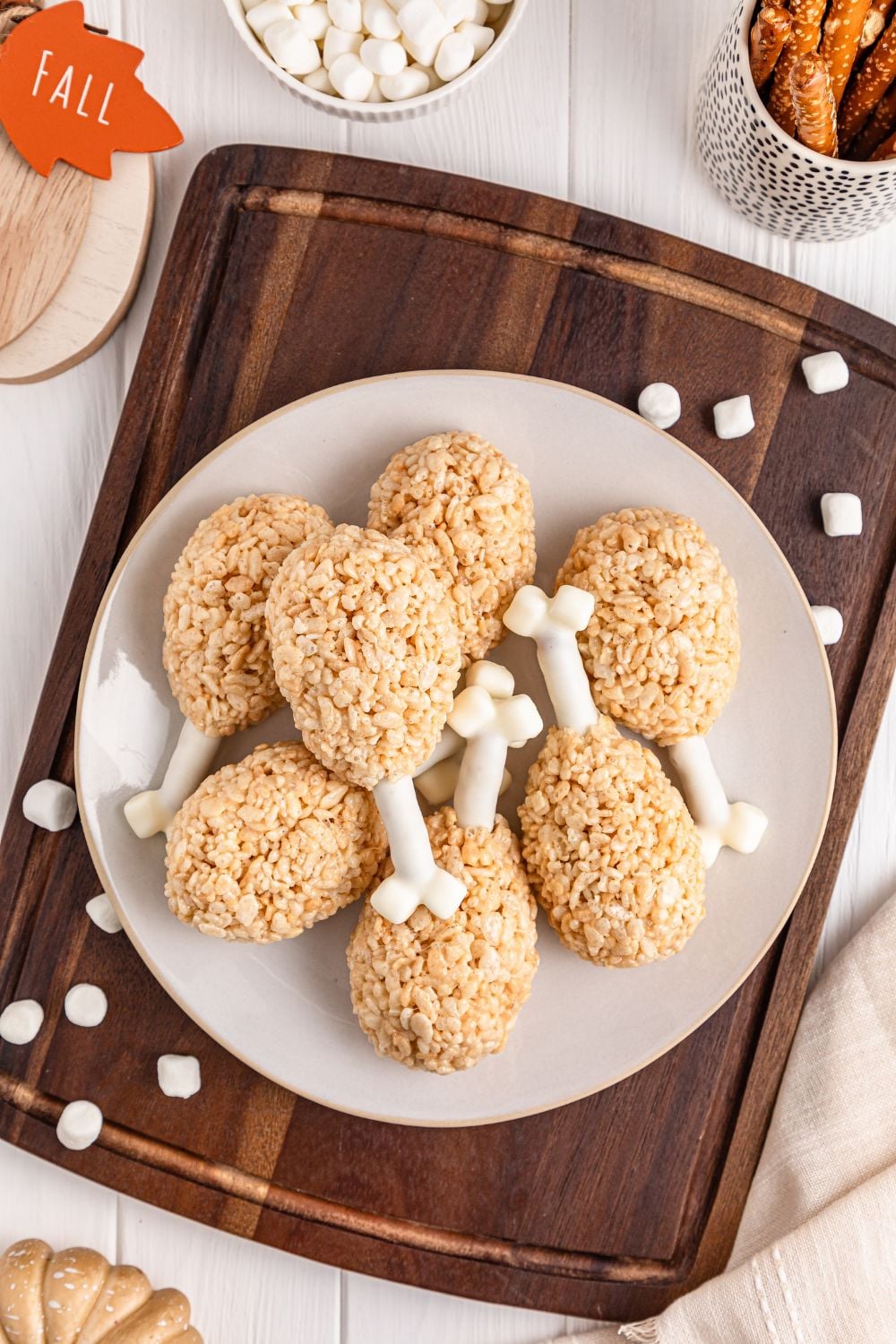 Rice Krispie Treat Turkey Legs sitting on a platter on the table on a plate with holiday decor scattered on table