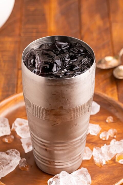 Witches Brew Cocktail mixture in a shaker glass with ice sitting on a tray