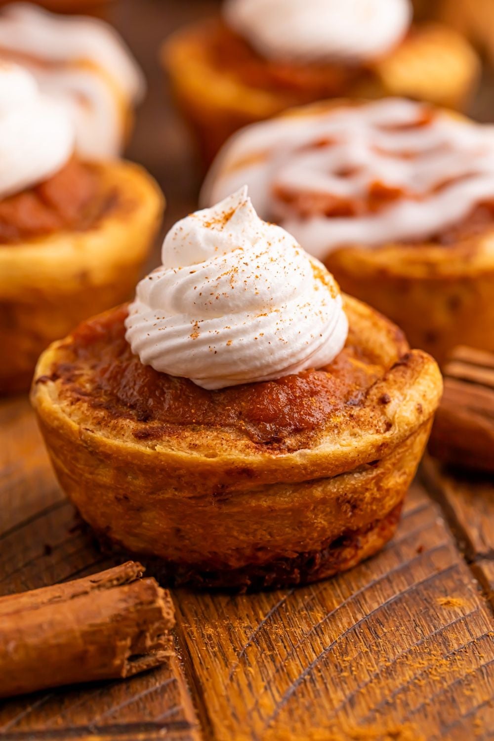 Pumpkin Pie Cinnamon Roll Cup on table with a dollop of whipped cream and pumpkin spice sprinkled on top