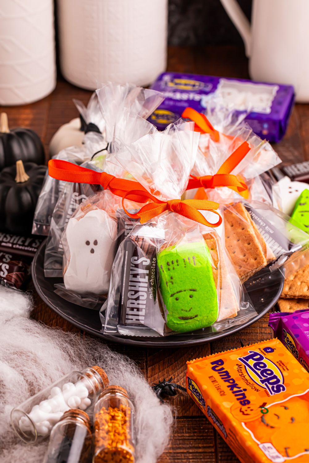 Halloween Smores Gift Bags on a plate with fake spider web and bags of marshmallows on table around to show ingredients in bags 