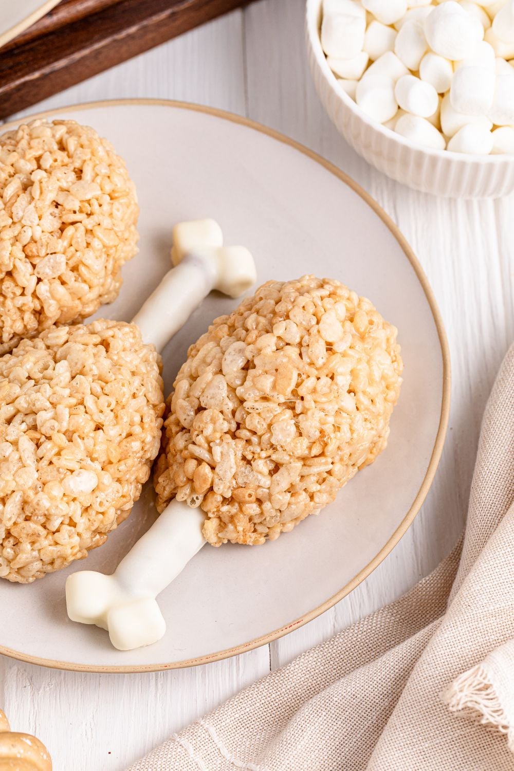 Rice Krispie Treat Turkey Legs on a white plate with bowl of mini marshmallows to the side