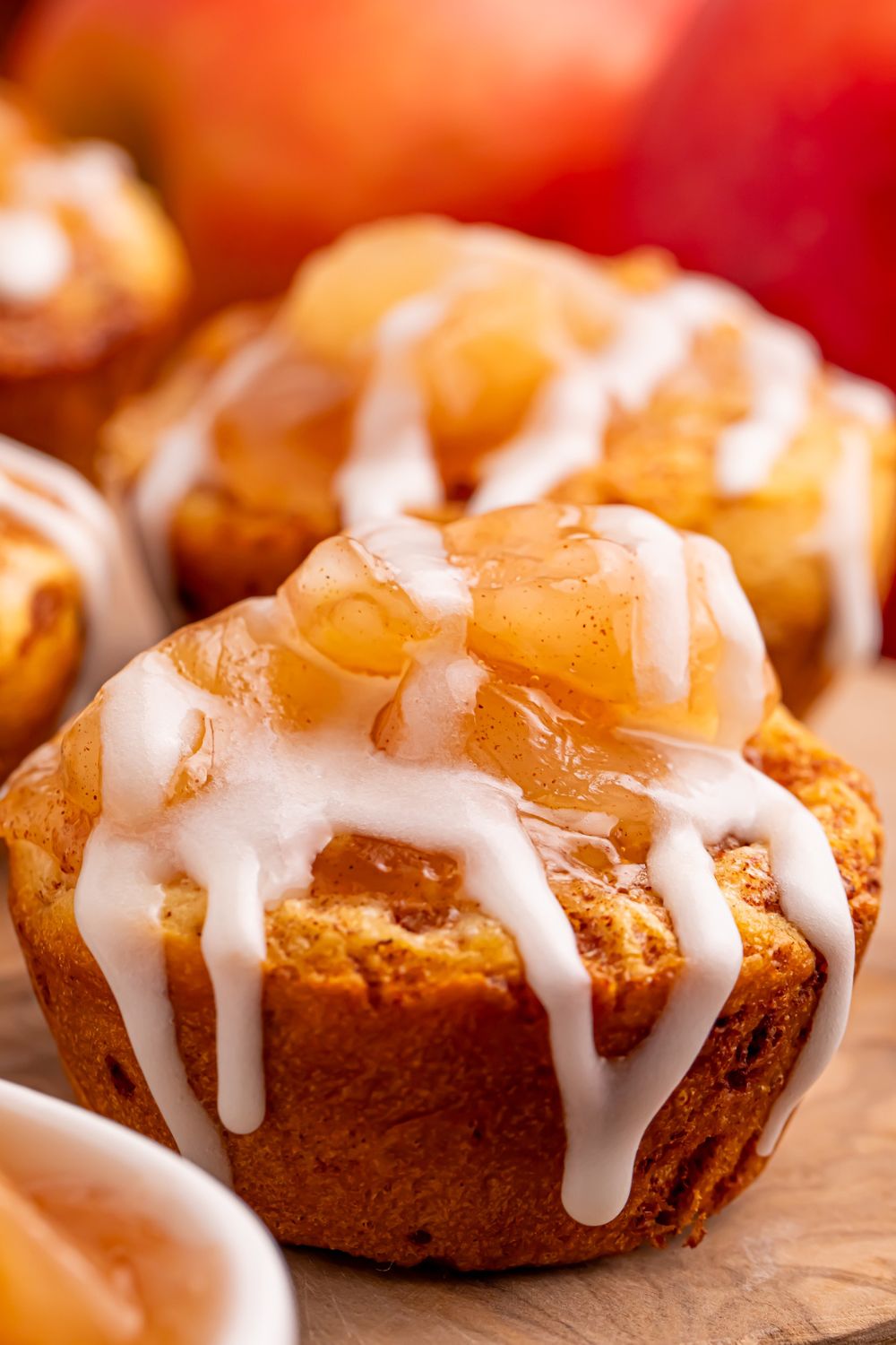 mini apple pies muffin cups on a table with a close up of the icing drizzling down the sides of the cinnamon rolls