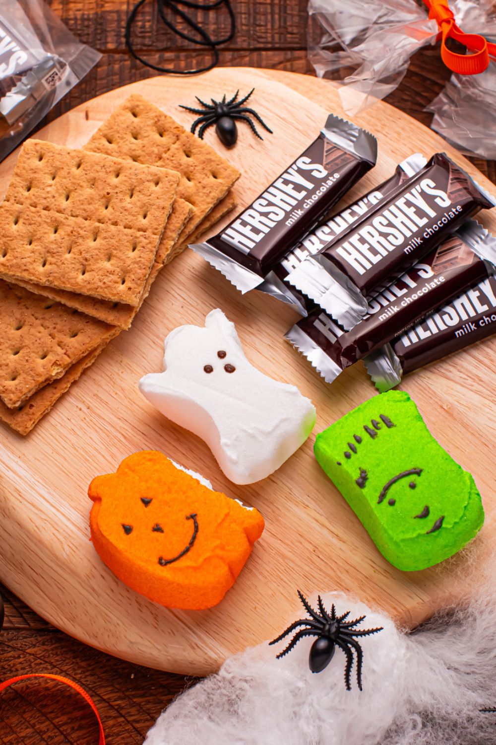 Halloween Smores Gift Bag ingredients on a round cutting board with plastic spiders and halloween decor around it 