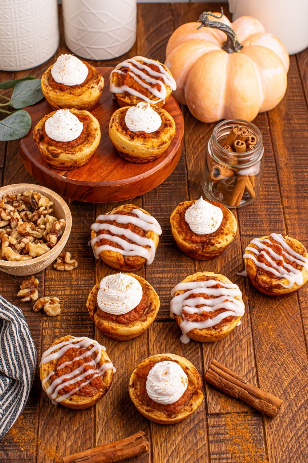 Pumpkin Pie Cinnamon Roll Cups spread out all over the table with cinnamon sticks and other ingredients around the cups