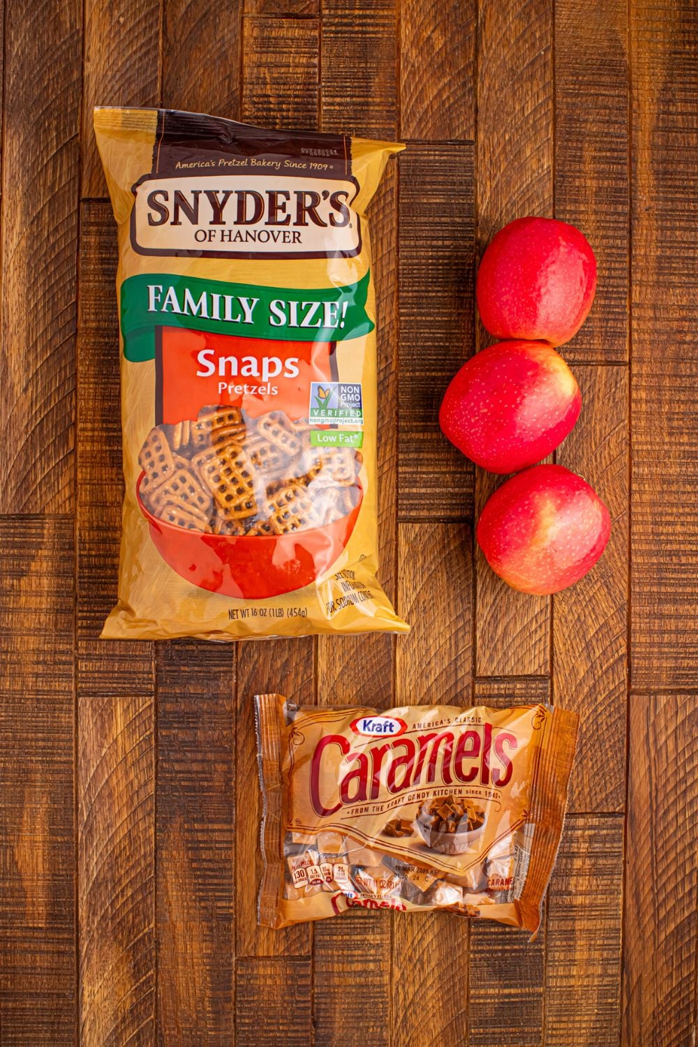 Caramel Apple Pretzel Bite ingredients on wooden table: bag of pretzels, apple, caramels in bag