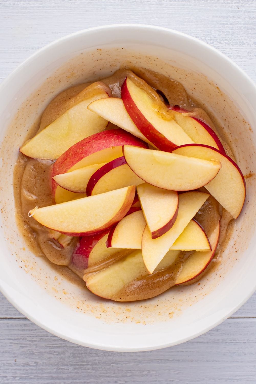 sliced apples in a butter mixture sitting on table in a white bowl