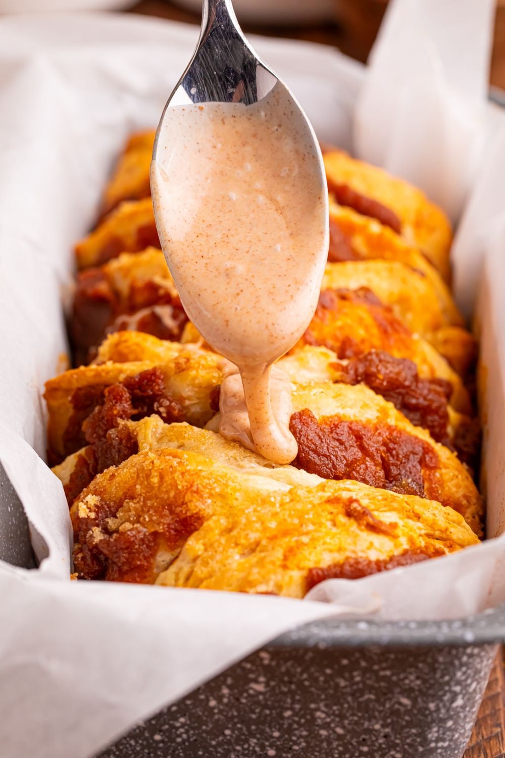 maple glaze being drizzled on top of the baked Pumpkin Pie Pull Apart Bread