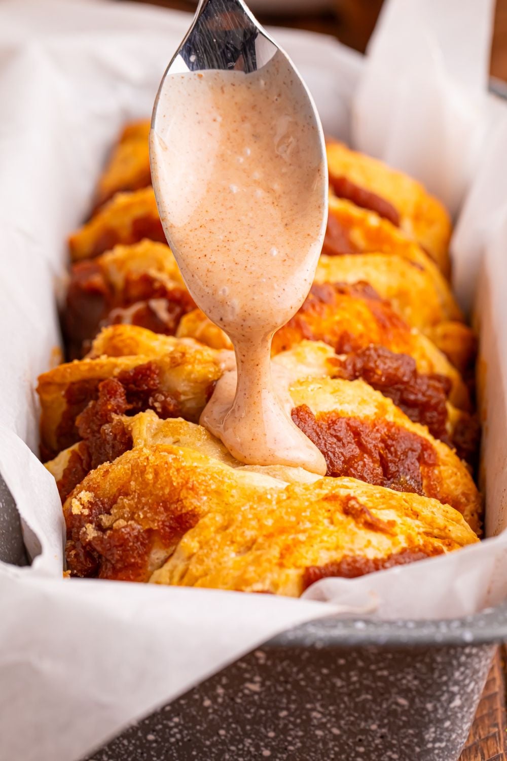 pumpkin pull apart bread in pan with a maple glaze being drizzled on top with a spoon