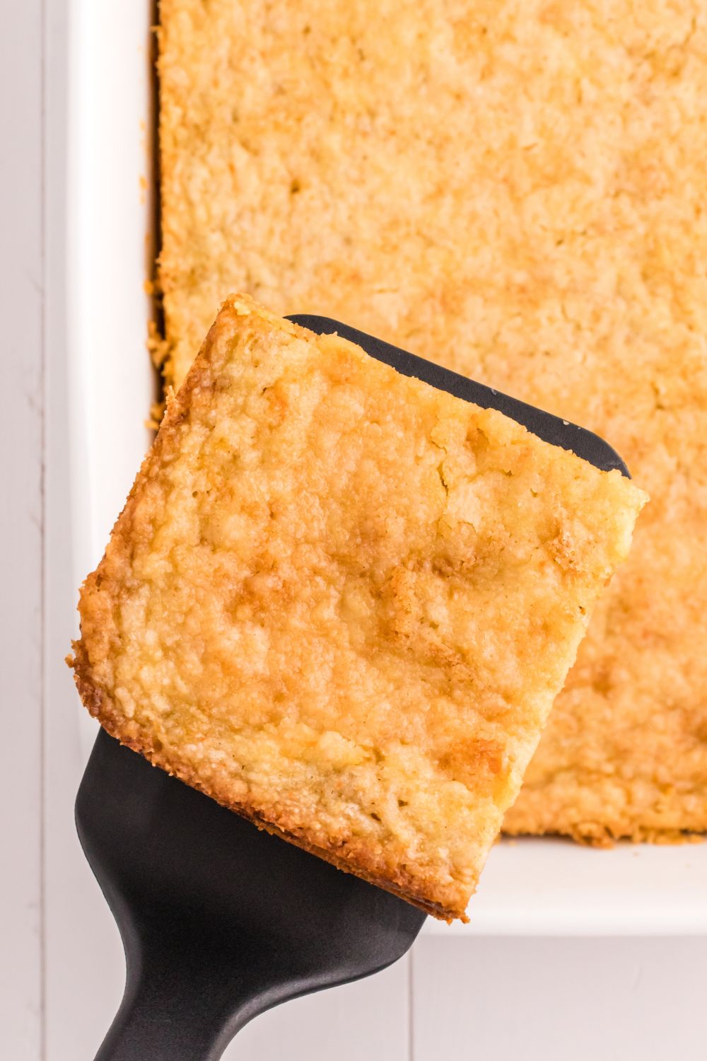 cake slice on a spatula above pan with cake