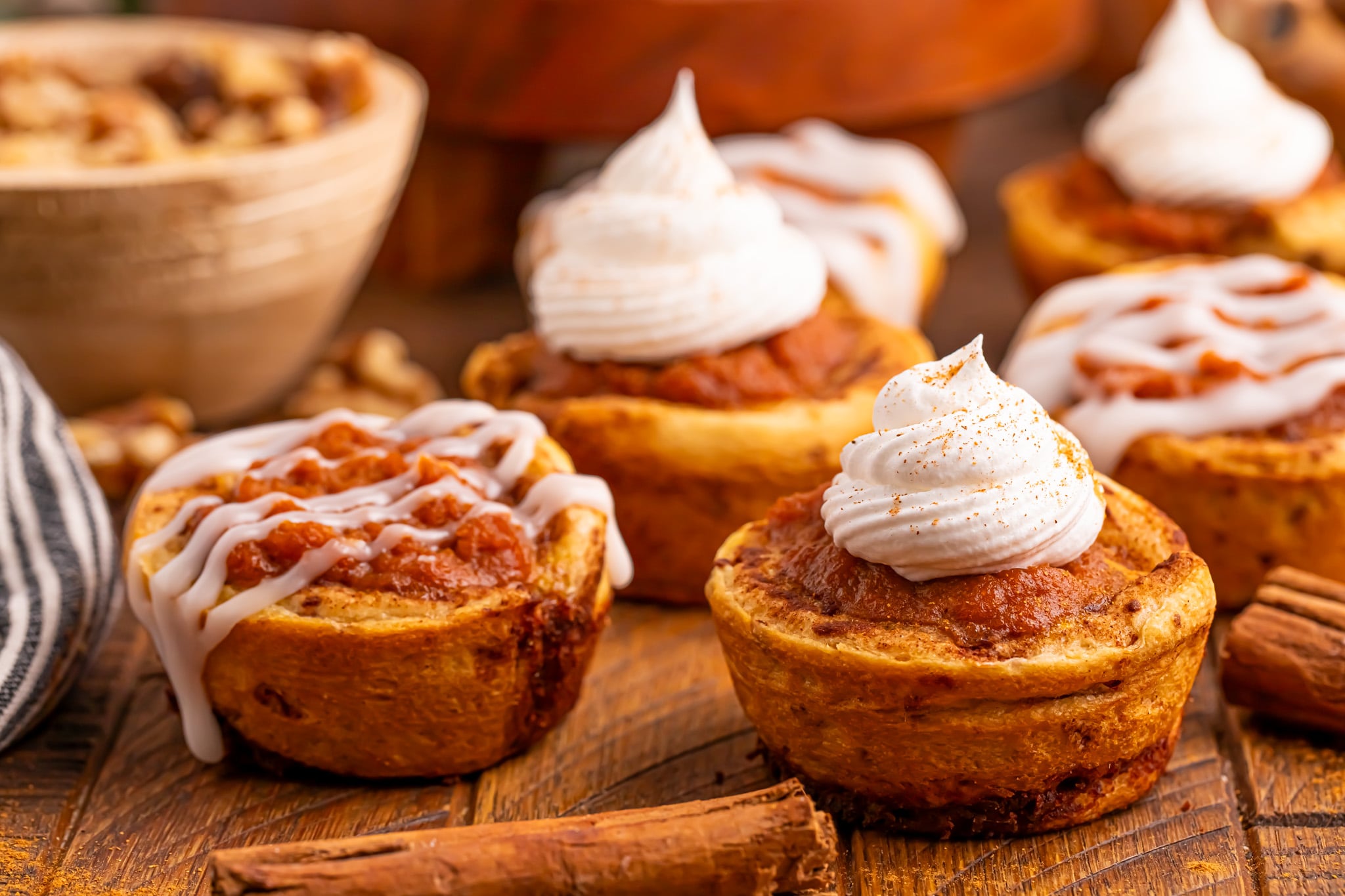 Pumpkin Pie Cinnamon Roll Cups with a cinnamon roll glaze drizzled on top sitting on table
