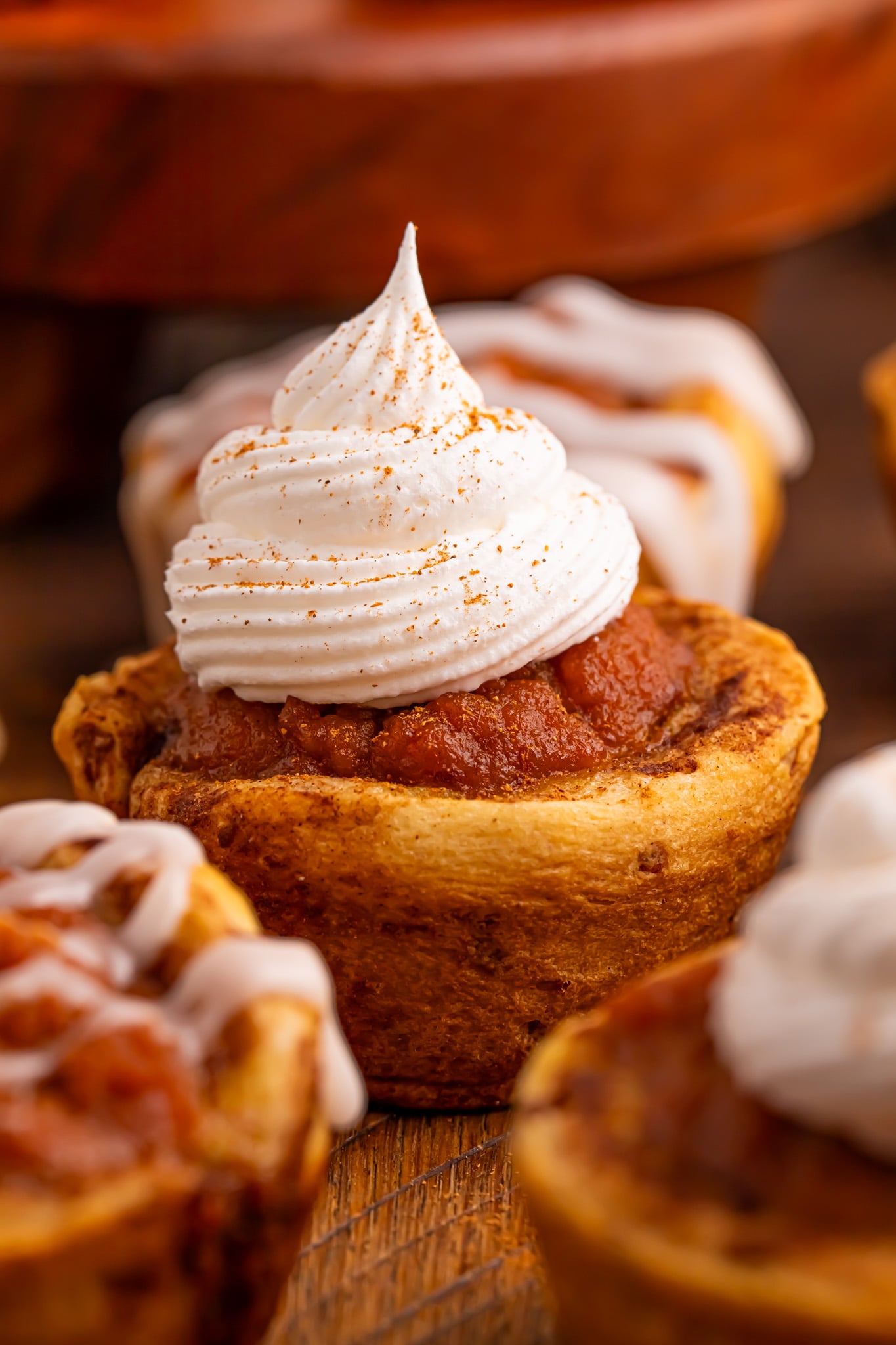 Pumpkin Pie Cinnamon Roll Cups on table with whipped cream on top of some and a icing glaze on others